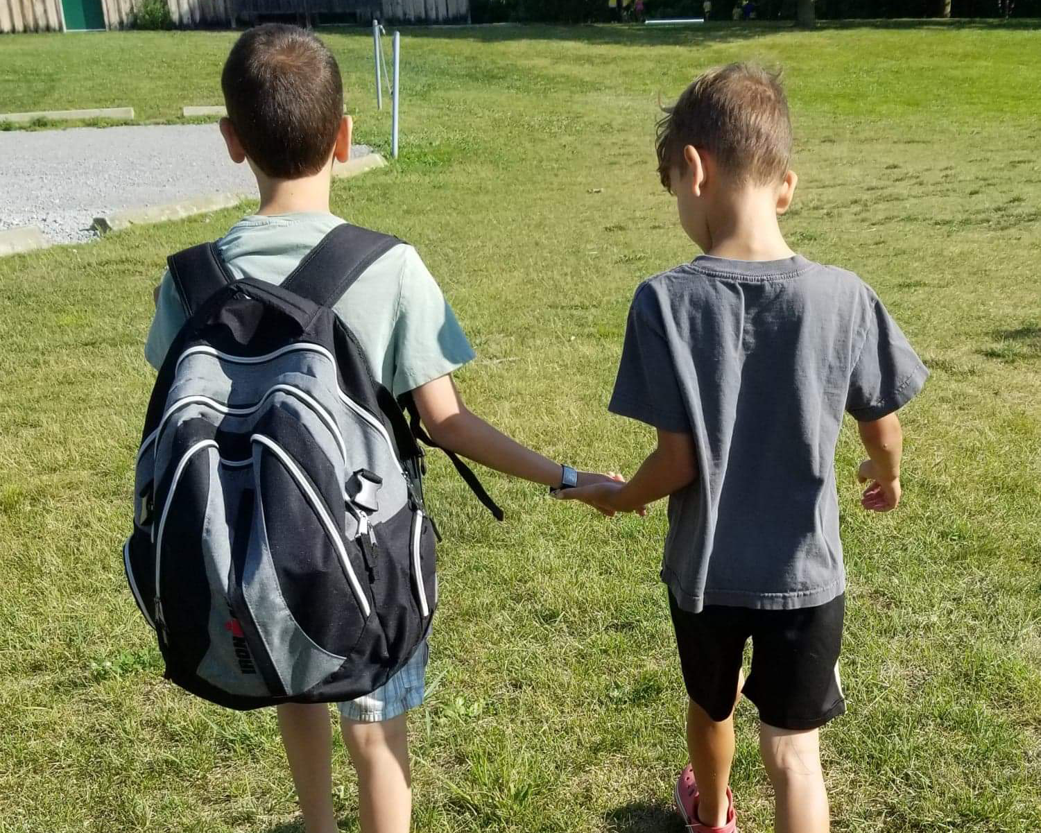 Two boys holding hands and walking outside on grass.