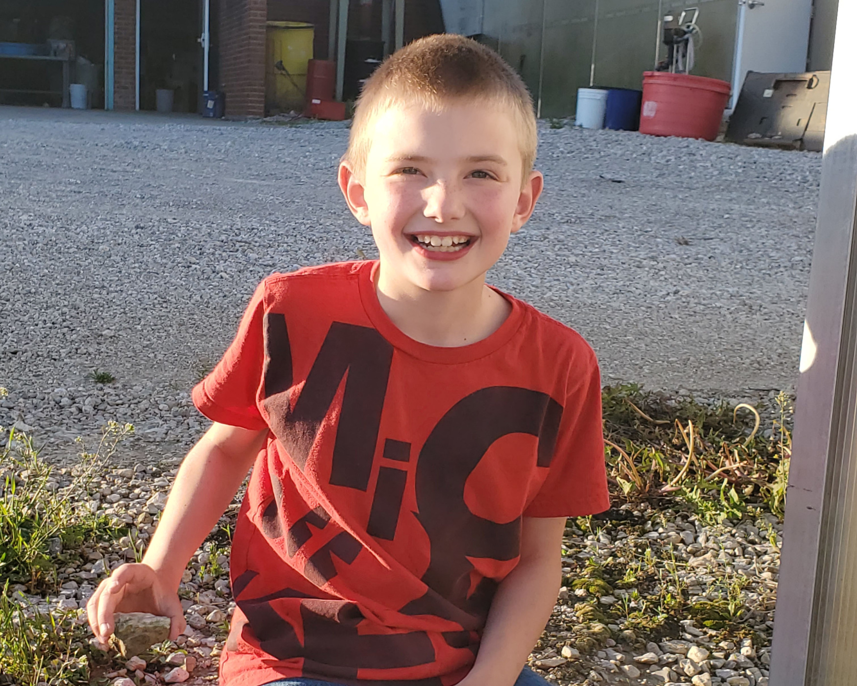 Boy smiling and sitting by a road.