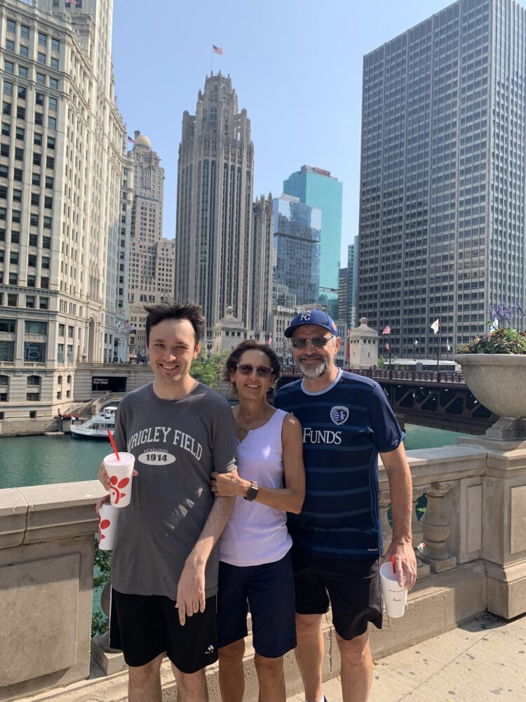 Boy and his parents in a city with water and tall buildings behind them.