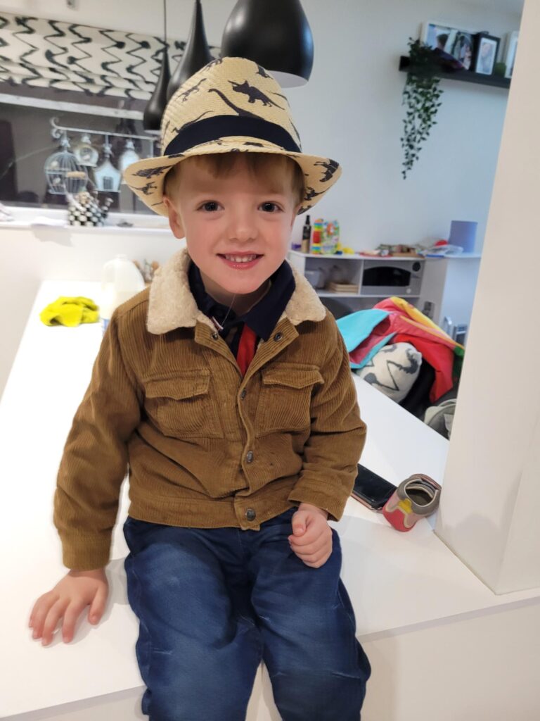 Oscar smiling with a dinosaur hat on.